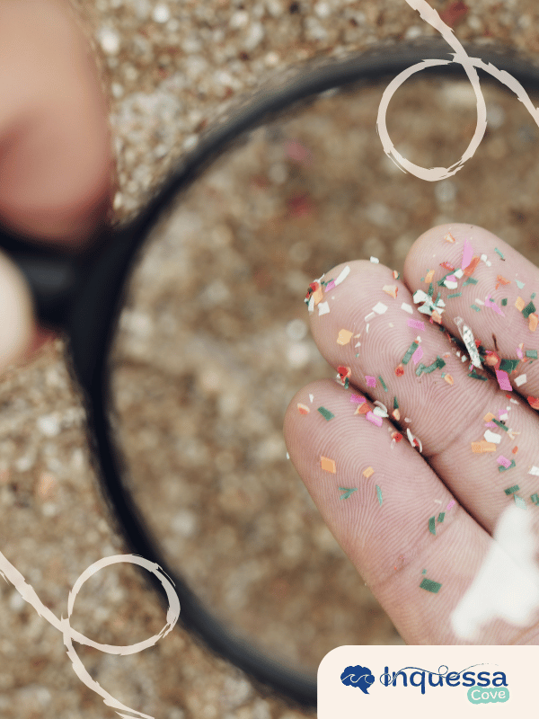 Tiny colorful plastic fragments resting on a person's fingertips under a magnifying glass