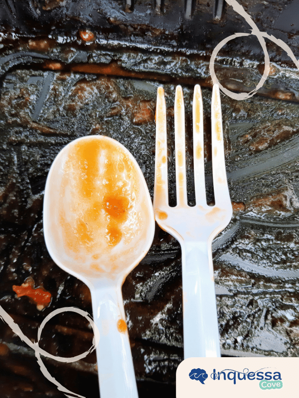 White plastic spoon and fork with food residue on a dark tray