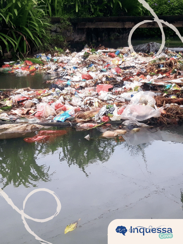 Large pile of plastic and other trash beside a polluted river
